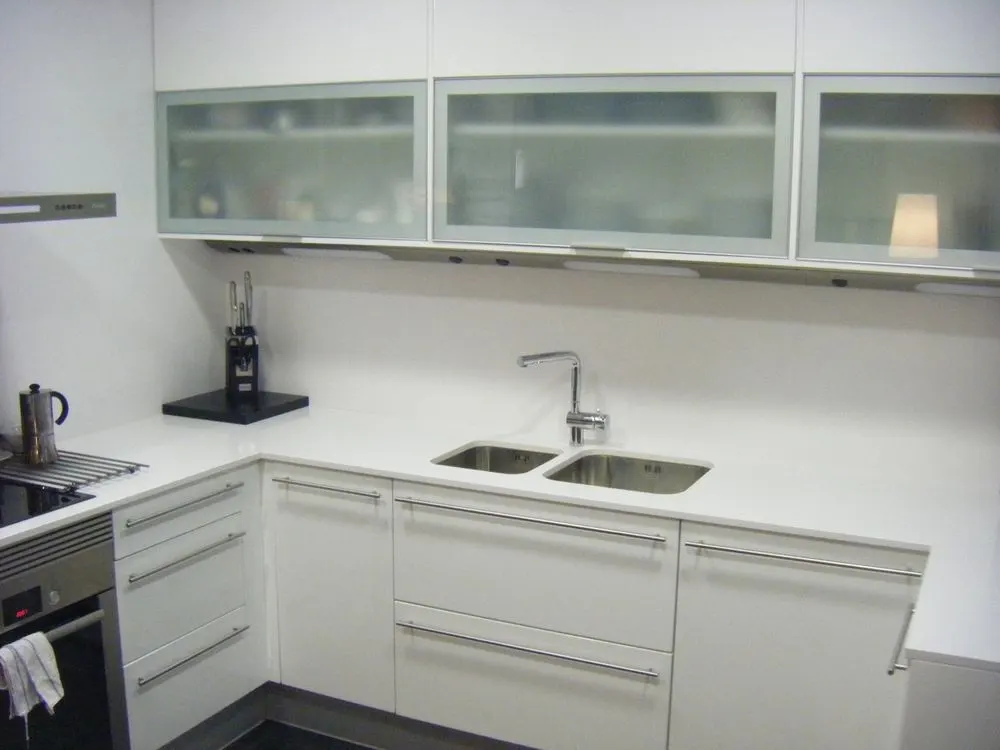 Cocina en L blanca con encimera clara y muebles altos de cristal